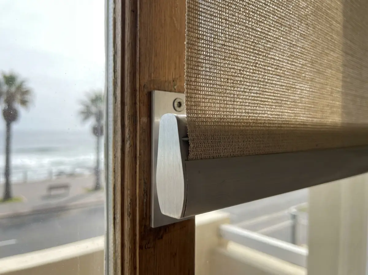 Close-up of a sunscreen roller blind fabric edge and aluminium bracket at a window in an older sectional-title apartment along the Sea Point promenade